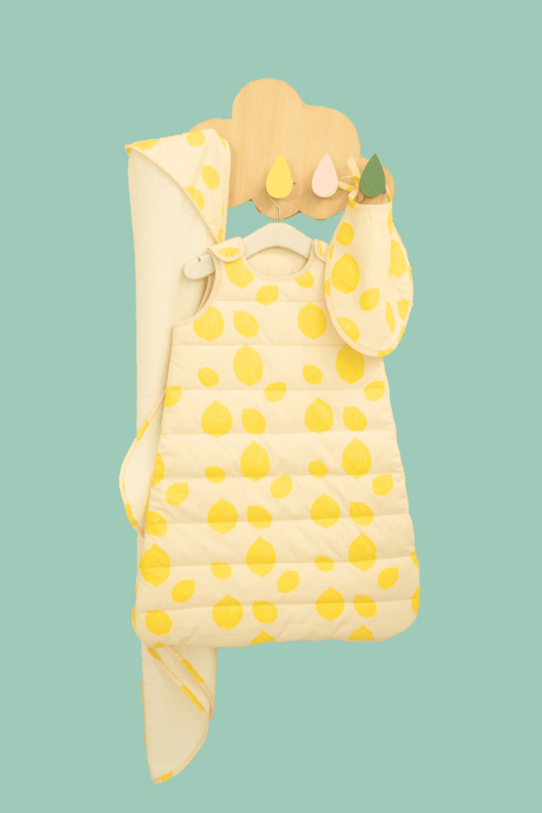 La gigoteuse, le bavoir et la cape de bain au motif Lemon sont suspendu à un crochet en forme de nuage, collection bébé naissance en coton bio Baby Care