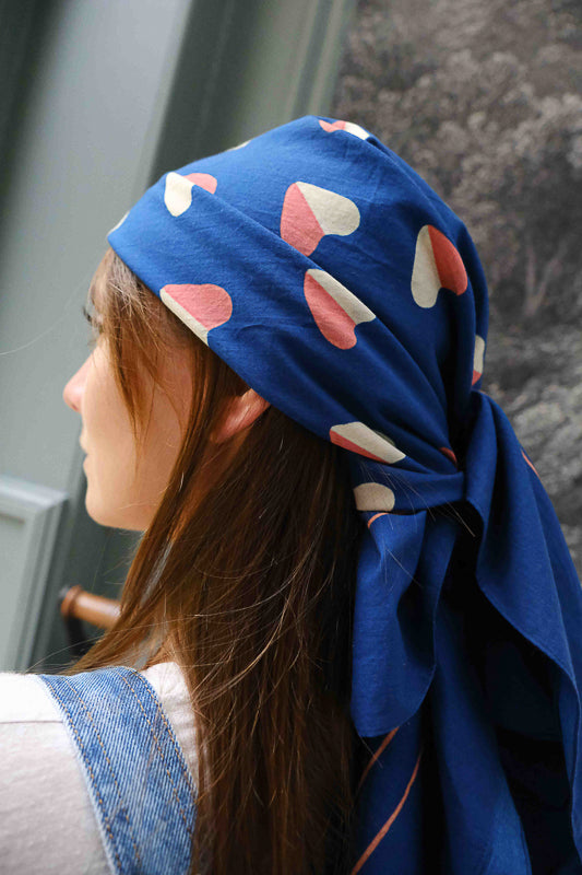 Foulard pour femme porté en accessoire pour les cheveux. Tissu en coton imprimé cœur sur fond bleu. Accessoire mode pour femme en coton, 130x130cm.