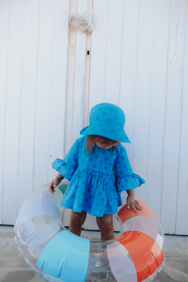 Bébé portant le BOB et la blouse PIA bleus motifs cœurs verts, vêtements bébé en coton bio certifié GOTS style vintage mixte