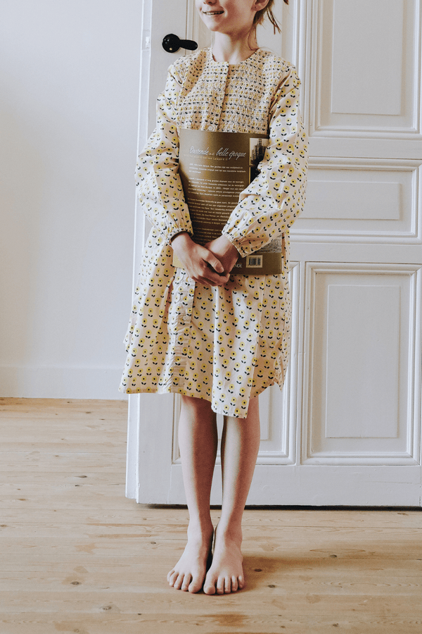 Enfant portant la robe ALMA coupe longue à manches longues boutonnée sur le devant couleur beige motif fleurs jaunes en coton bio certifié GOTS style vintage