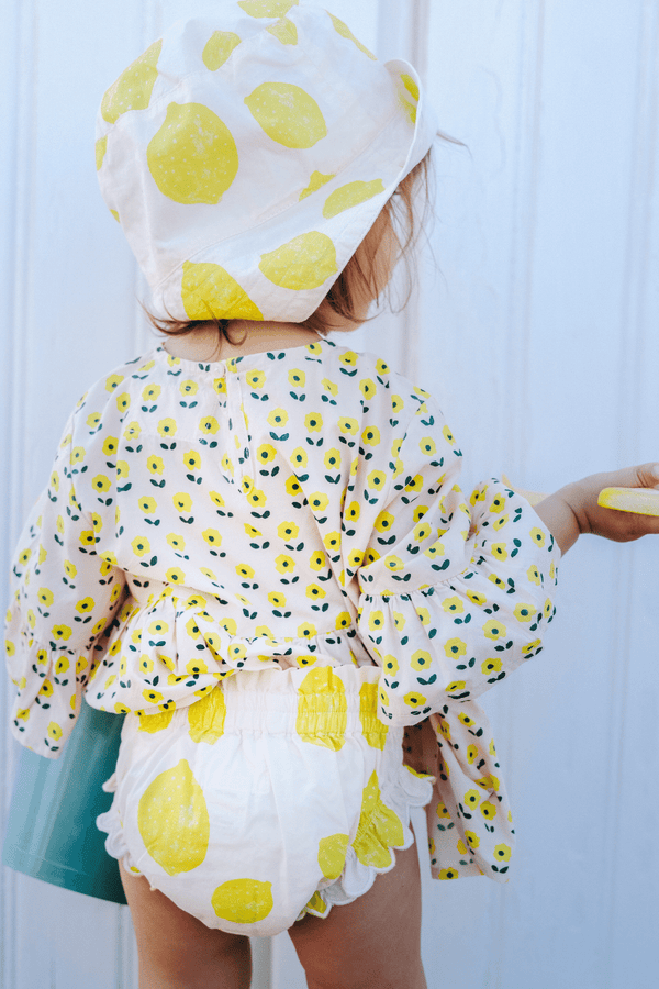 Bébé portant la blouse PIA imprimé petites fleurs jaunes, le bloomer BETTY motif citron et le BOB assorti, vêtements bébé en coton bio certifié GOTS style vintage mixte unisexe
