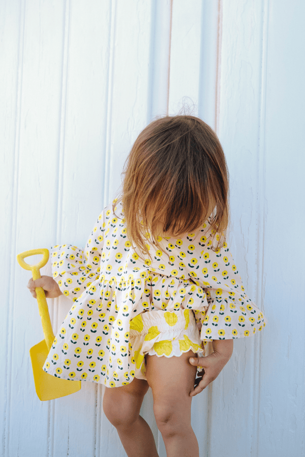 Bébé portant la blouse PIA imprimé petites fleurs jaunes et le bloomer BETTY motif citron, vêtements bébé en coton bio certifié GOTS style vintage mixte unisexe