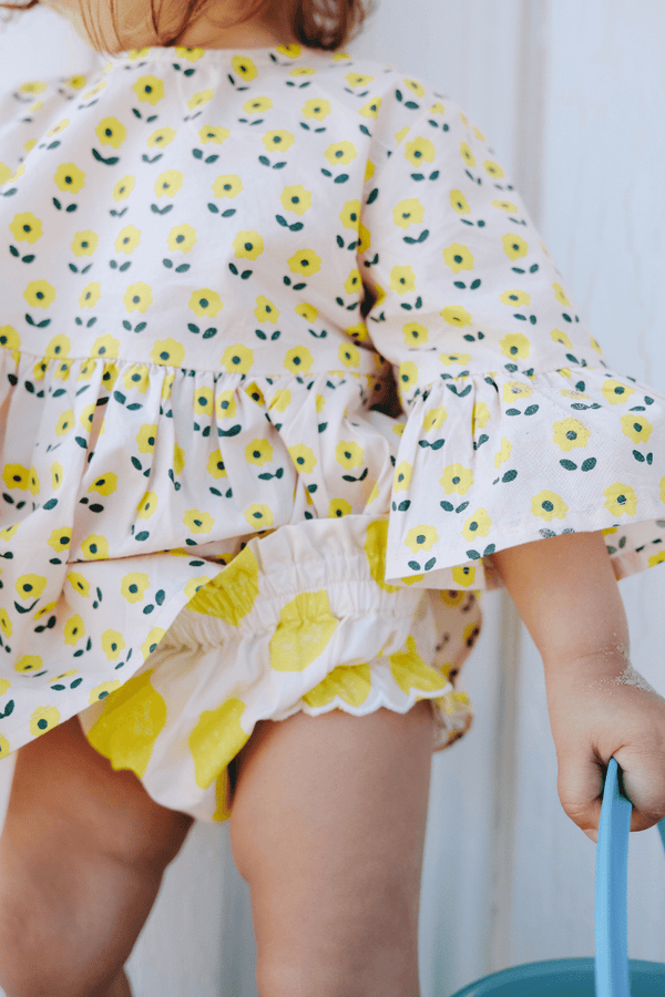 Bébé portant la blouse PIA imprimé petites fleurs jaunes et le bloomer BETTY motif citron, vêtements bébé en coton bio certifié GOTS style vintage mixte unisexe