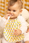 Bébé joyeux jouant avec une petite cuillère, qui porte le bavoir à motif Flower en coton bio de la capsule bébé naissance Baby Care