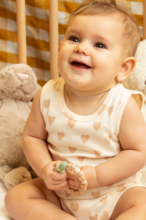 Beau bébé souriant avec un jouet dans ses mains, portant le body de la collection bébé naissance Baby Care en coton bio.