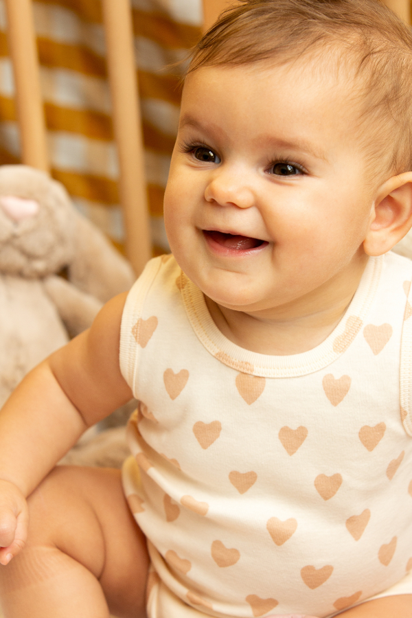 Bébé riant habillé d'un body au motif cœur beige en coton bio, collection bébé naissance Baby Care