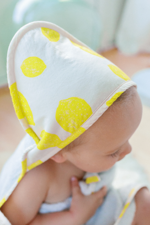 Bébé enveloppé dans la cape de bain en coton bio de la capsule bébé naissance Baby Care au motif citron